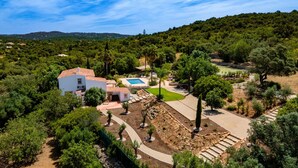 Eine Villa mit Swimmingpool, umgeben von üppiger Vegetation und einer hügeligen Landschaft.