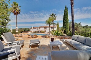 A poolside area with lounge chairs, a stone table, and a view of a house in the background.