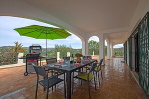 Un patio al aire libre con una mesa lista para comer, una parrilla y un paraguas verde.