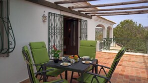 Une terrasse avec une table dressée pour deux personnes, des chaises vertes et une vue sur la campagne.