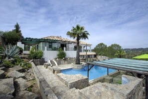 Un espace piscine avec des marches en pierre menant à la piscine, le tout entouré d’un bâtiment blanc doté d’un toit en tuiles et d’un palmier.