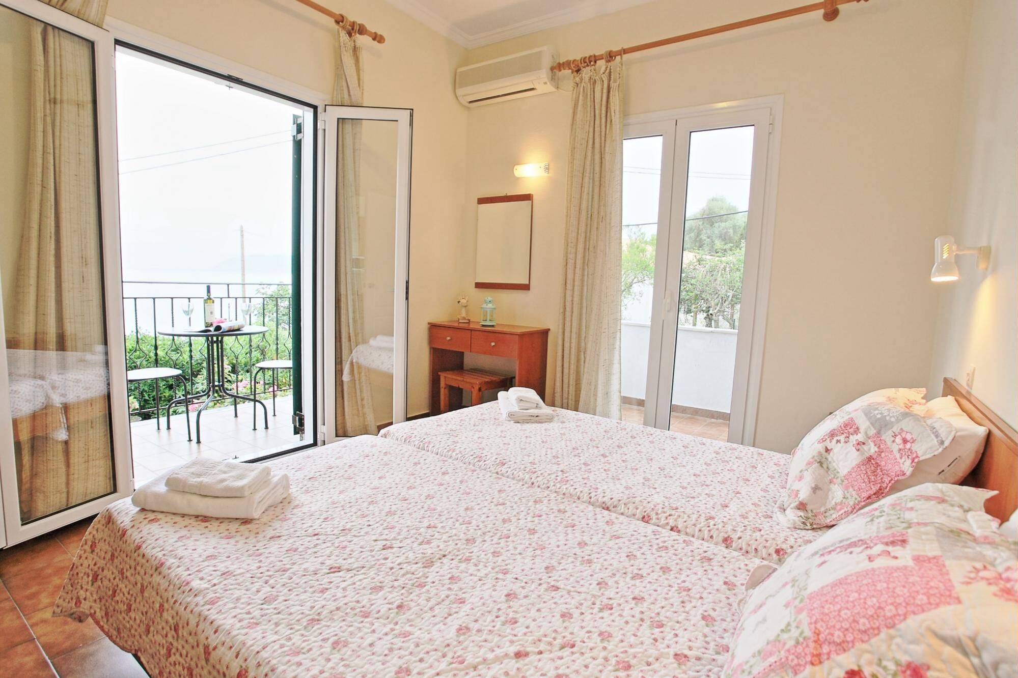 Un dormitorio con cama, mesita de noche, cómoda, espejo y balcón con mesa y sillas.