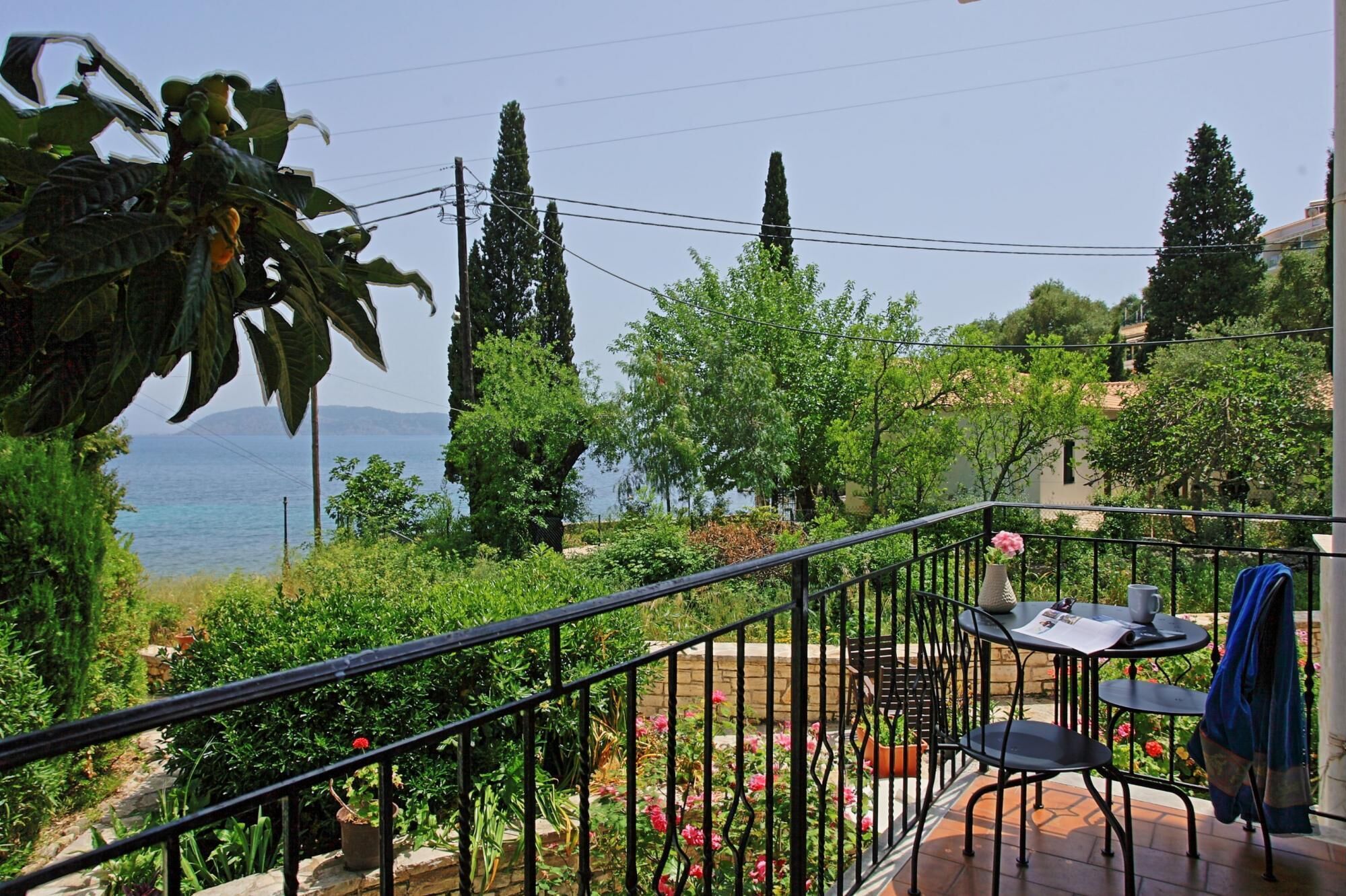 A balcony with a view of the sea, surrounded by greenery and a stone wall.