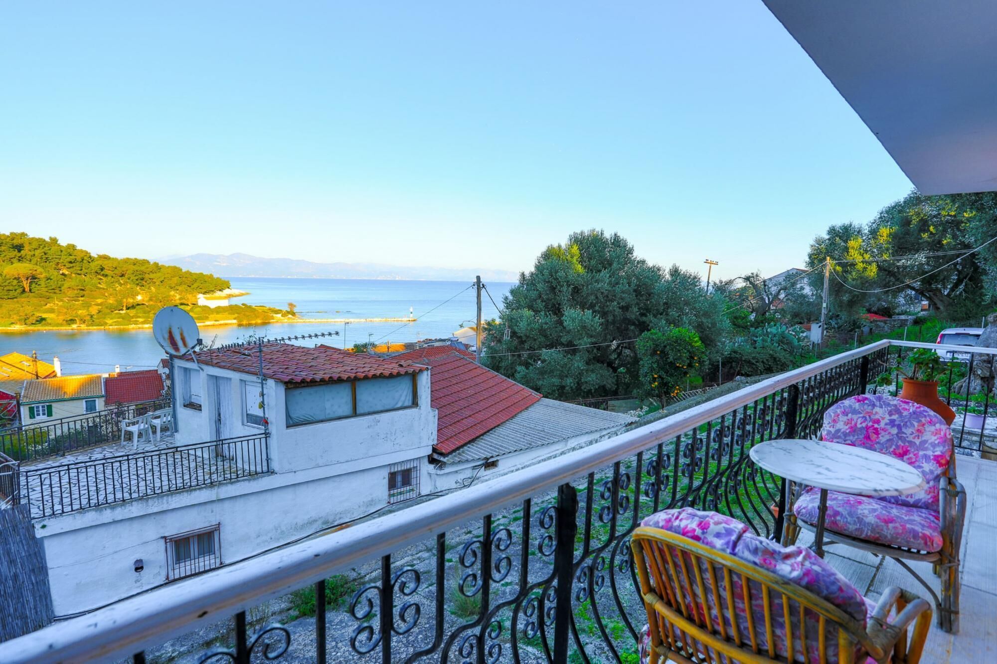 Un balcon donnant sur une étendue d’eau, une antenne parabolique et une chaise avec un coussin à motifs floraux.