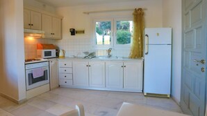 Een kleine keuken met witte kastjes, een magnetron, oven, spoelbak en koelkast.