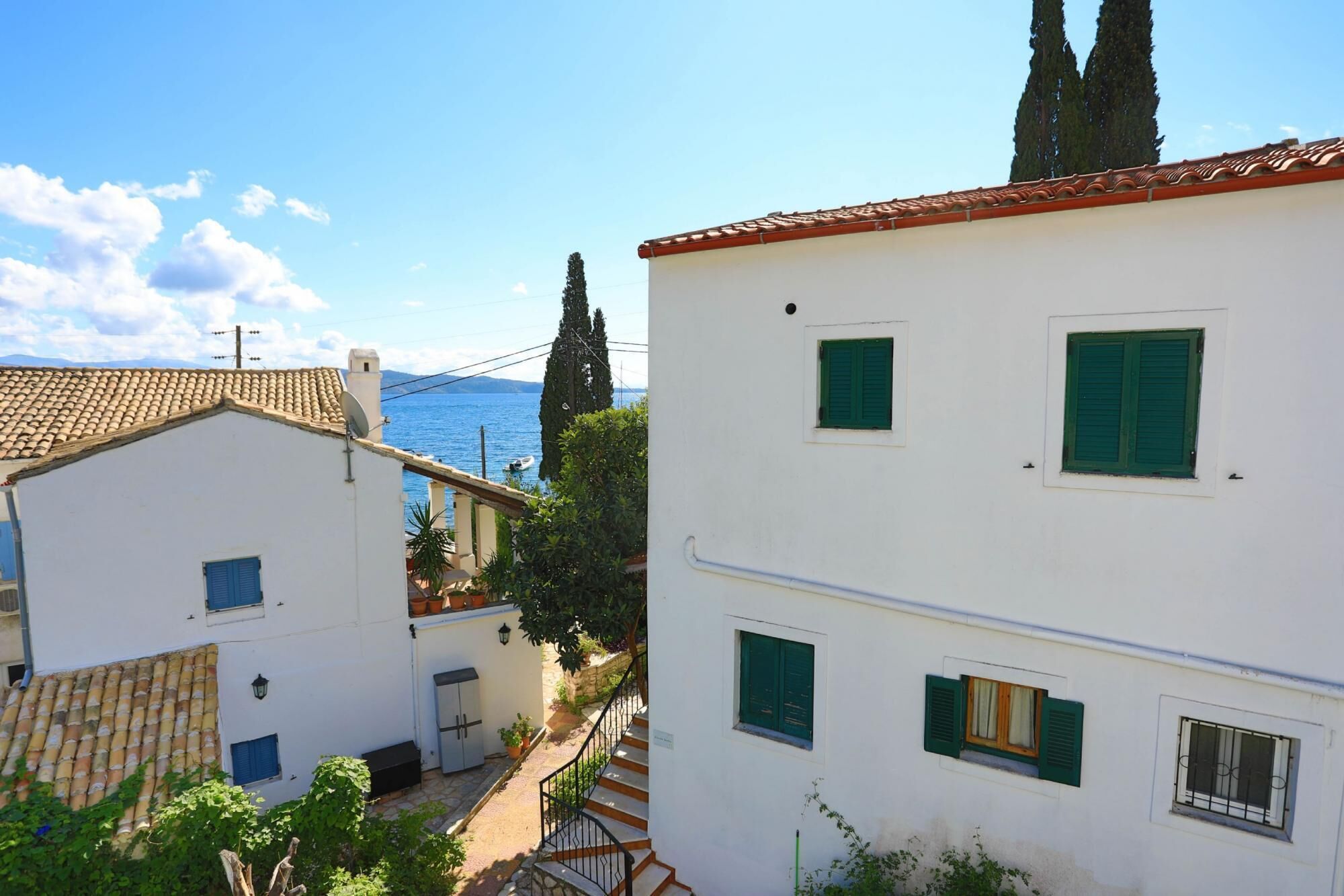 Um edifício branco com persianas verdes, telhado de azulejos e vista para o mar.