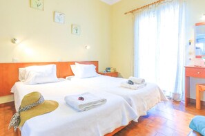 Quarto de hotel com duas camas, cabeceira de madeira, mesa de cabeceira e banheiro com espelho e pia.