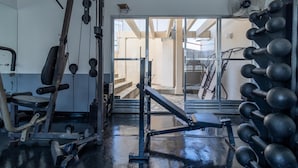 A gym with exercise equipment, a fan, and a view of a building through a glass door. - Br156166 Sirio Libanes (São Paulo)