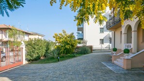A paved courtyard with a building on one side and a fence on the other. - Villa Mimosa - Appartamento 2 (Desenzano del Garda)