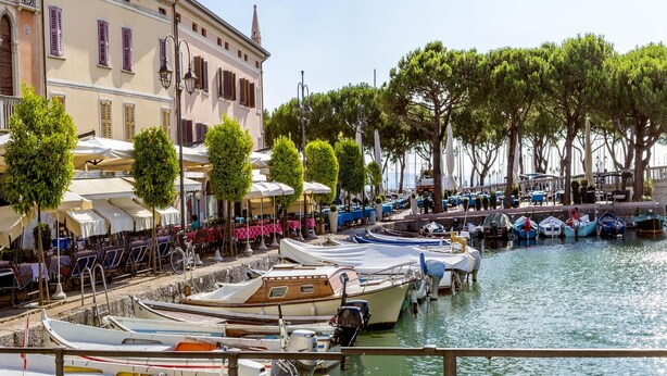 A waterfront area with boats docked, outdoor seating, and a building with a clock tower. - Villa Mimosa - Appartamento 2 (Desenzano del Garda)