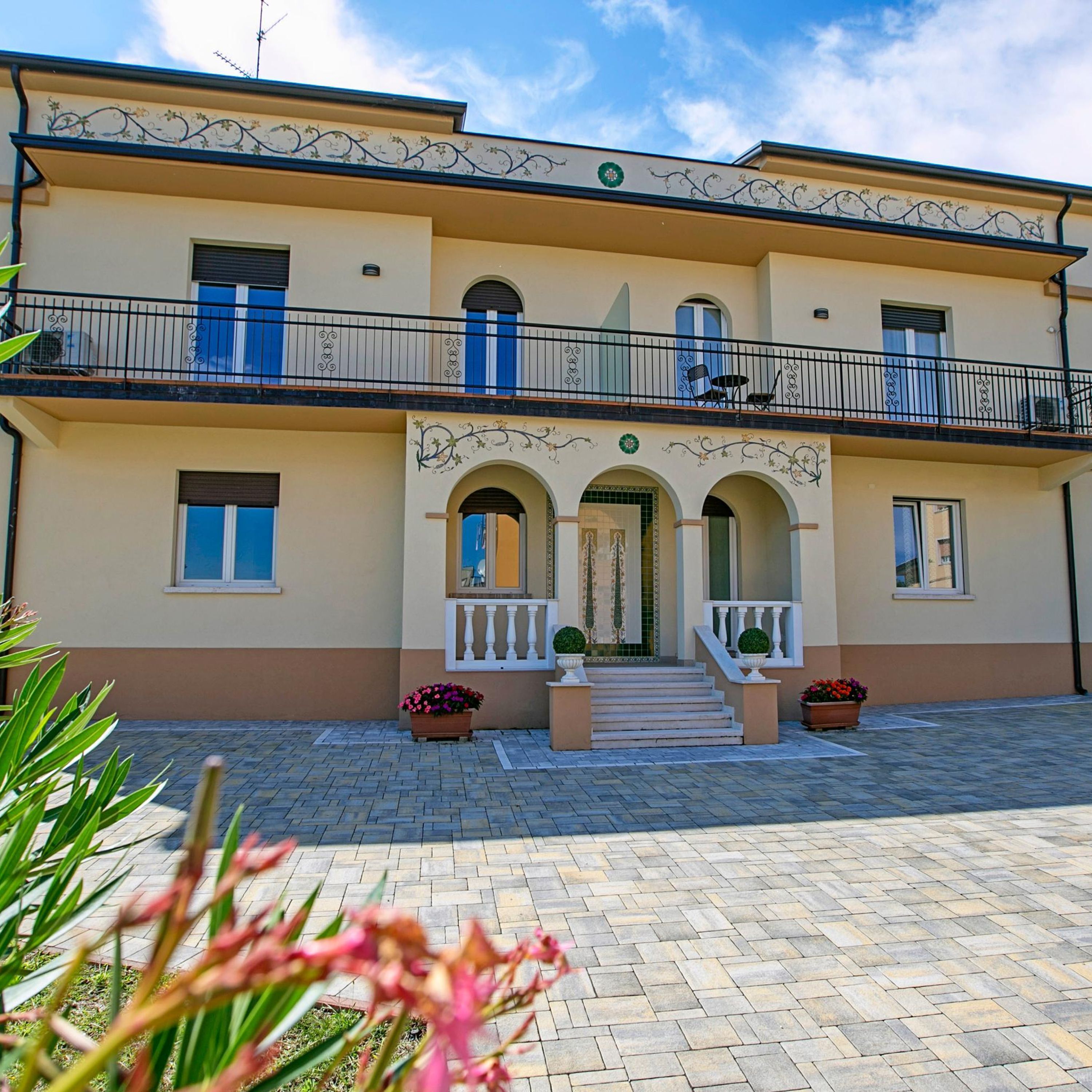 A two-story building with a central entrance, a balcony on the upper floor, and a paved courtyard.
