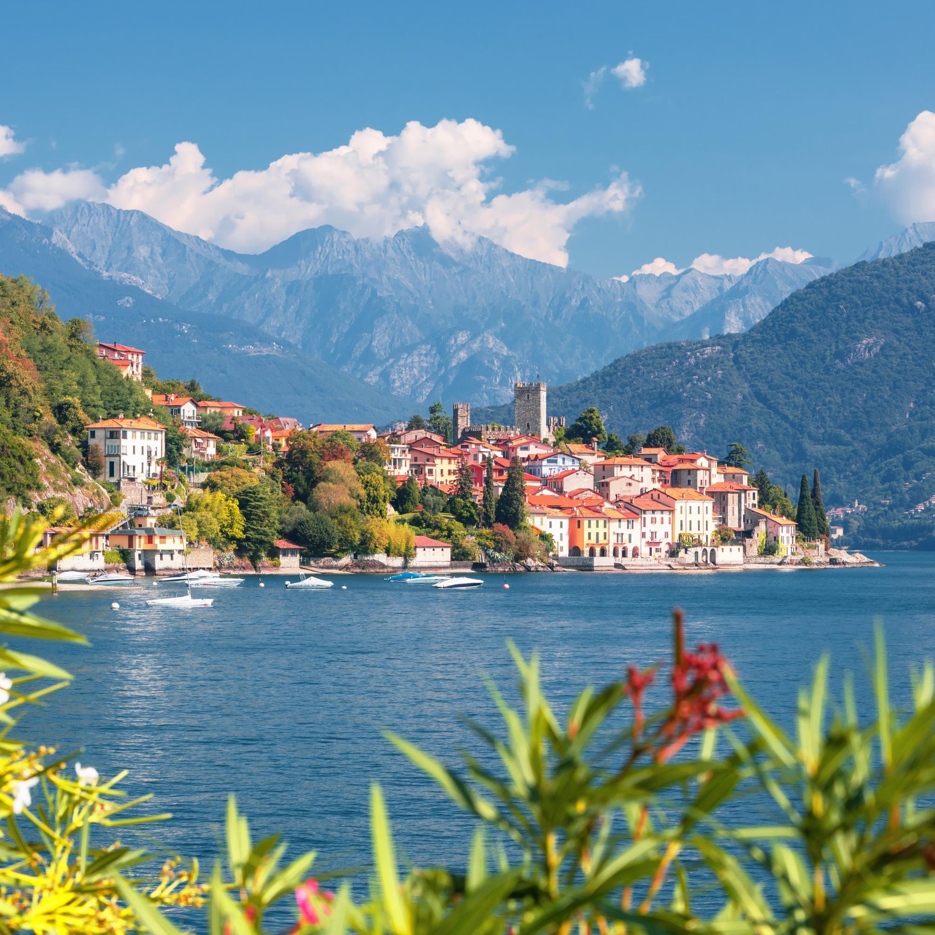 A coastal town with buildings on a hillside overlooking a lake, surrounded by mountains.