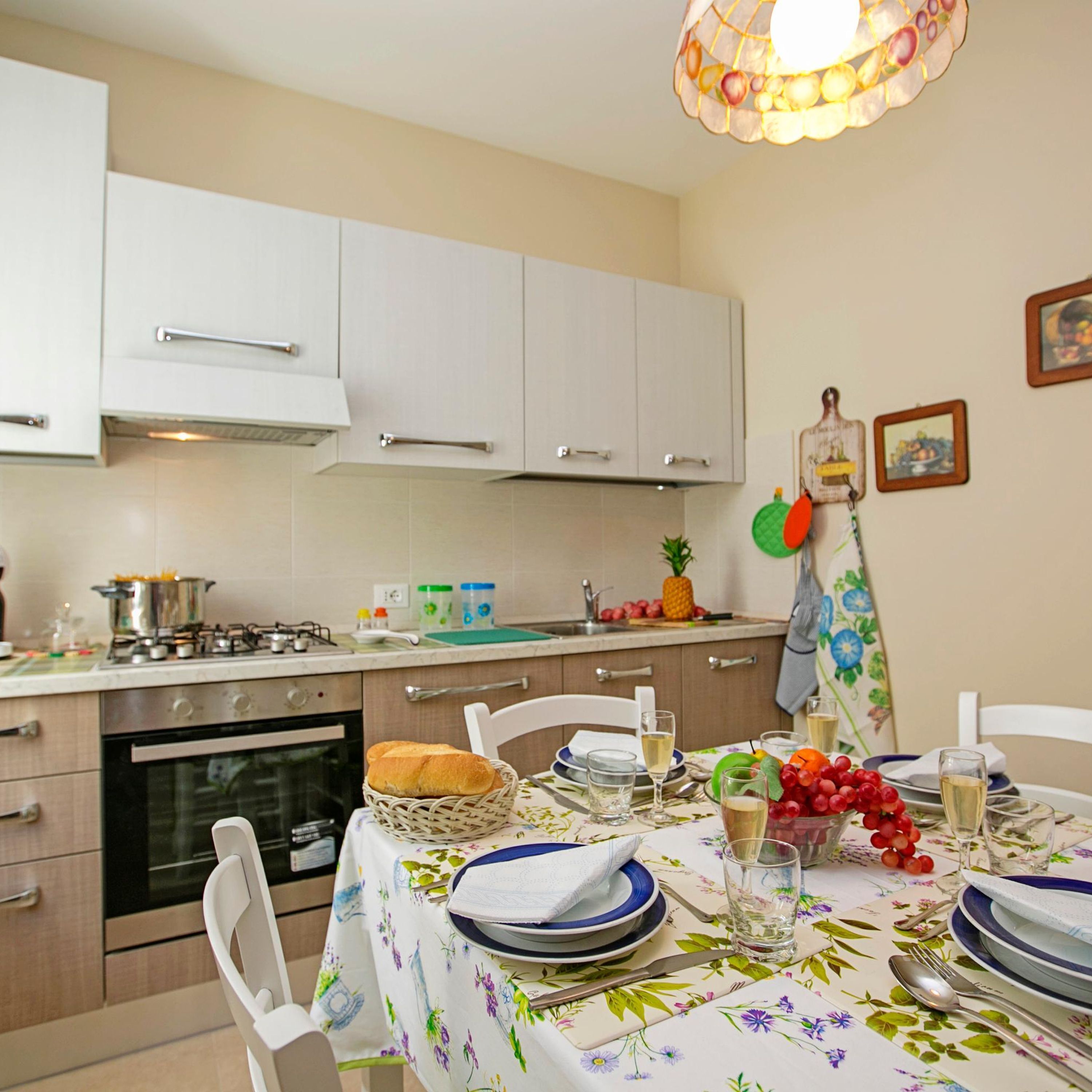 A modern kitchen with white cabinets, a gas stove, and a dining area set with plates, glasses, and a basket of bread.