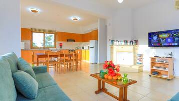 Una sala de estar moderna con un sofá, una mesa baja con fruta, una cocina con armarios de madera y un televisor montado en la pared.