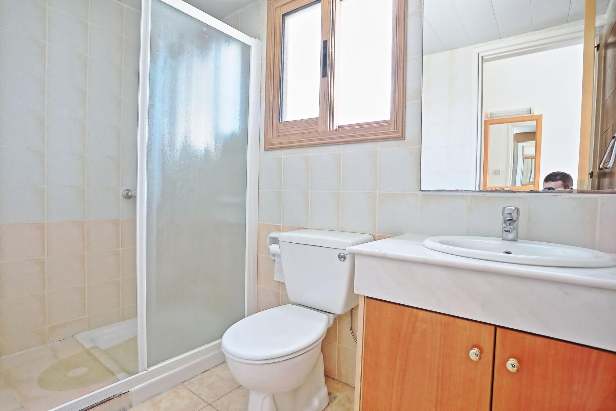 Un bagno con box doccia in vetro, un water bianco, un lavabo con mobiletto in legno e uno specchio sopra il lavabo.