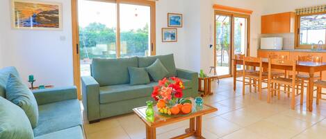 A living room with a sofa, a coffee table with fruit, and a kitchen area with a dining table and chairs.