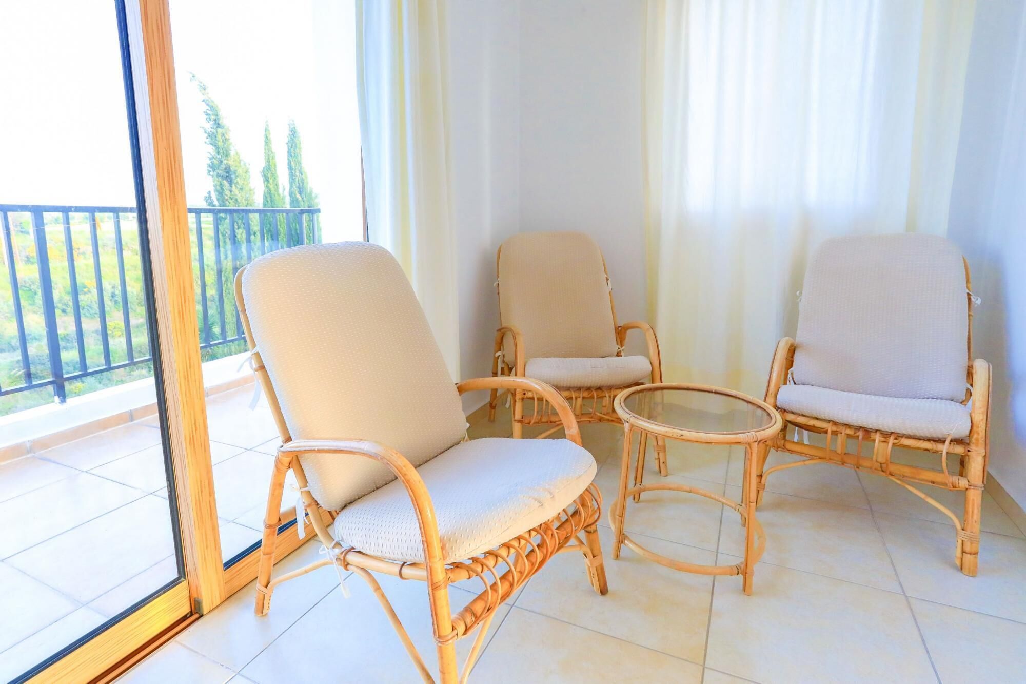 A balcony with three wicker chairs and a small glass table.