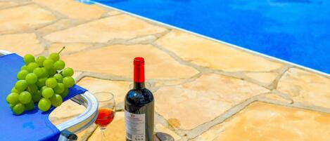 A poolside setting with a blue towel, a bunch of green grapes, a wine bottle, and a wine glass.
