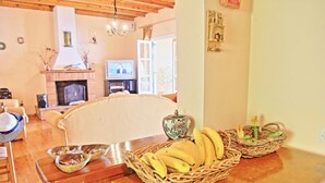 Ein gemütliches Wohnzimmer mit Kamin, Fernseher und Essbereich mit Korbwannen, die mit Früchten gefüllt sind.