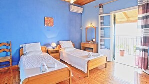 Ein Zimmer mit zwei Holzbett, einer Holzbalkendecke, einer blauen Wand, einem Fenster mit Vorhängen und einem kleinen Topfpflanzen auf dem Balkon.