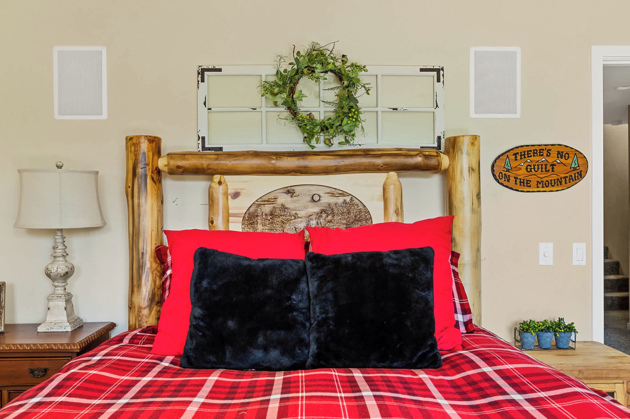 A bed with a red and black checkered bedspread, a wooden headboard, and a decorative wall hanging above it.
