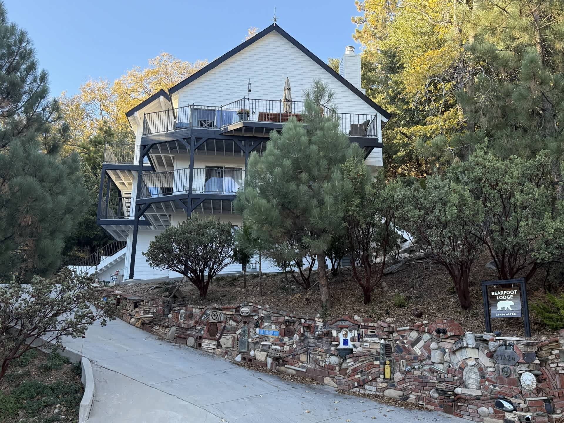 Un edificio de varios pisos con un balcón, rodeado de árboles y un muro de piedra con diversos objetos.