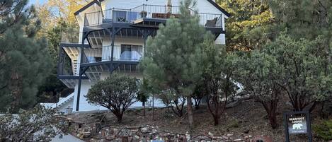 Un edificio de varios pisos con un balcón, rodeado de árboles y un muro de piedra con diversos objetos.