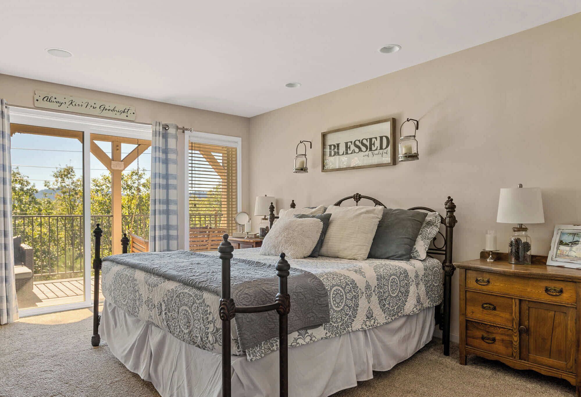 A bedroom with a bed, a nightstand, a dresser, a window with blinds, and a balcony.