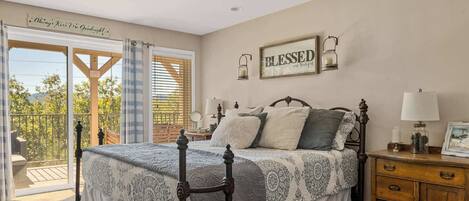 A bedroom with a bed, a nightstand, a dresser, a window with blinds, and a balcony.