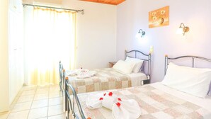 Une chambre avec deux lits, une fenêtre avec des rideaux, un tableau au mur et un ventilateur de plafond.