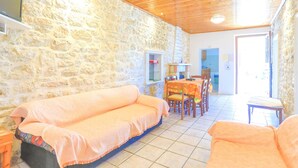 Une pièce chaleureuse avec un mur en pierre, un plafond en bois, un canapé, une table à manger avec des chaises et une petite table avec une lampe.