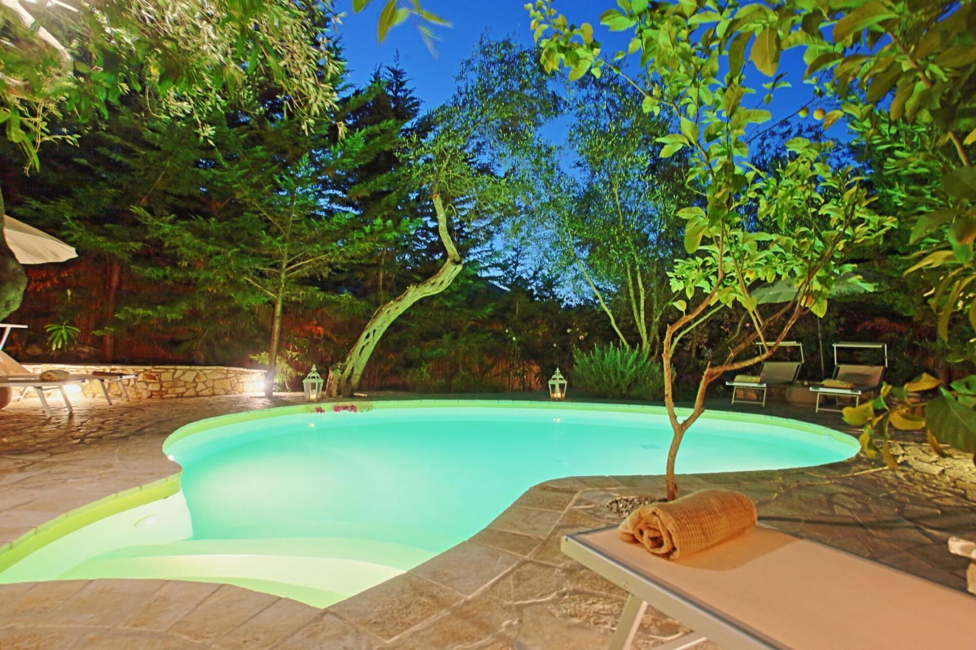 Une piscine bordée de pierres, entourée d’arbres et d’un mur de pierres.