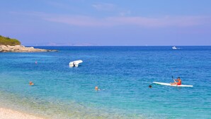 A beach with clear blue water, a rocky shoreline, and a person paddling a kayak. - Lili Luxury Cottage in Ozias (Paxos)