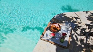A clear blue pool with a picnic setup on the edge, including a basket, a glass pitcher, and a bottle. - Lili Luxury Cottage in Ozias (Paxos)