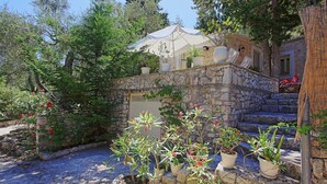 A stone building with a white canopy, surrounded by potted plants and trees. - Lili Luxury Cottage in Ozias (Paxos)