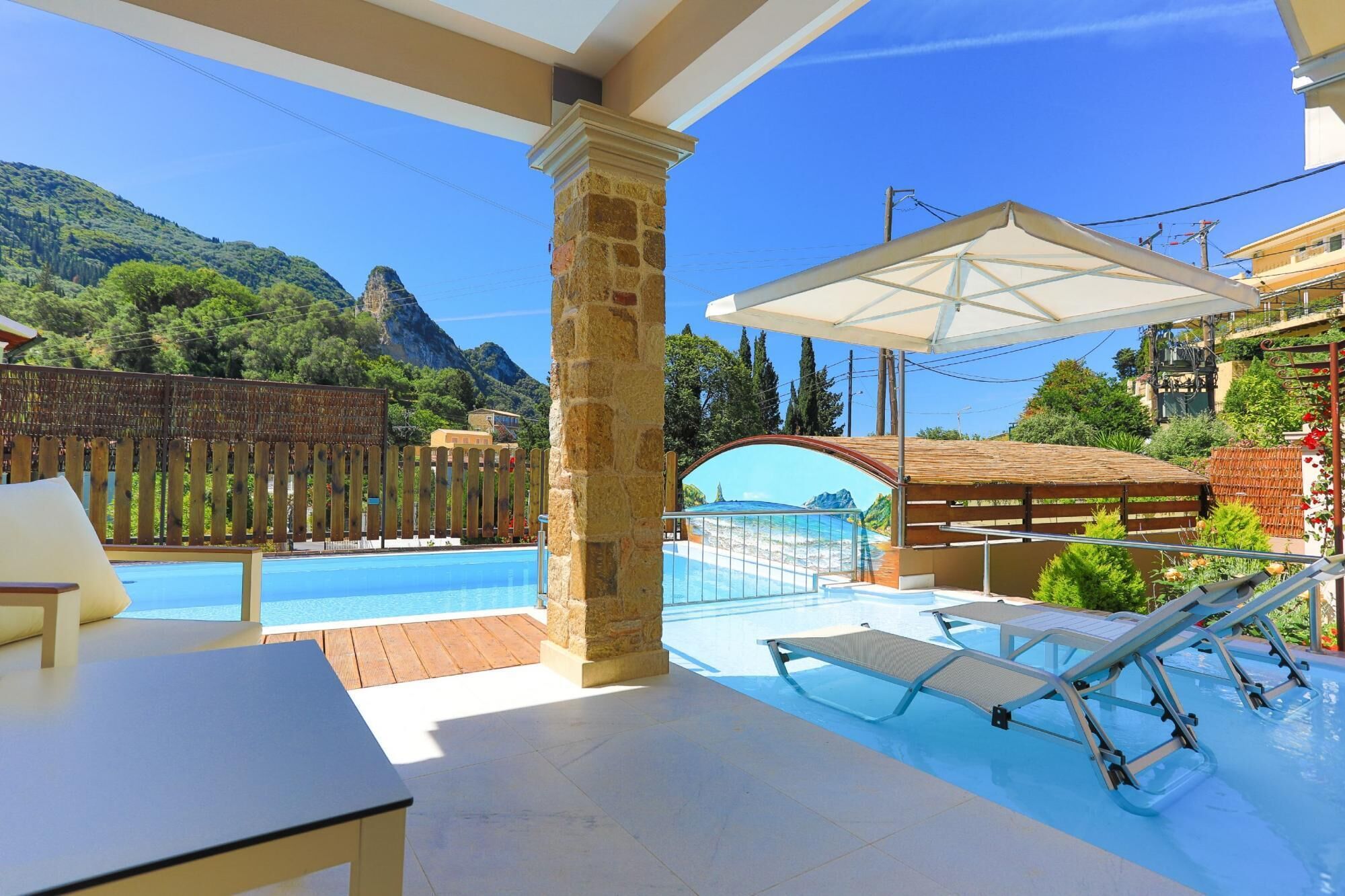 A pool area with lounge chairs, a wooden fence, and a mountain view.