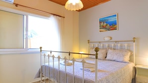 Ein Schlafzimmer mit weißem Metallbettgestell, einem Bild an der Wand und einem Fenster mit Vorhängen.