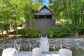 A cabin with a stone staircase leading to a dock, surrounded by trees and a small body of water.