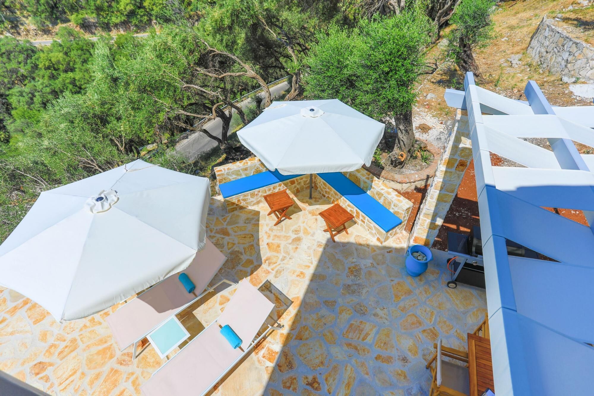 Une terrasse sur le toit avec un sol en pierre, des parasols blancs et des chaises en bois.