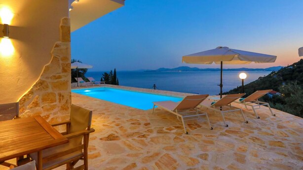 A stone pool with lounge chairs and umbrellas, overlooking a body of water and distant mountains. - Vista Mare Assinia in Kentroma (Corfu)