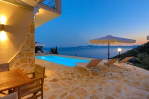 A stone pool with lounge chairs and umbrellas, overlooking a body of water with distant landforms. - Vista Mare Assinia in Kentroma (Corfu)