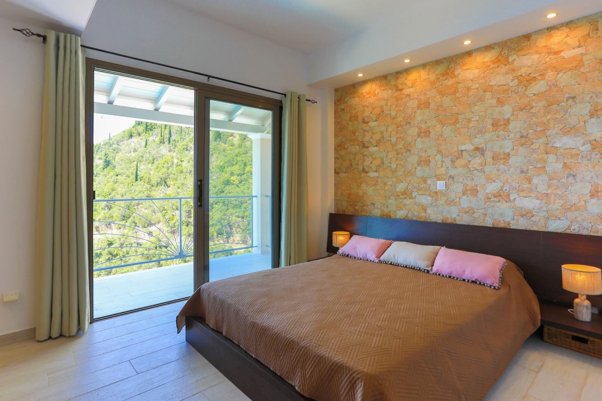 A bedroom with a large bed, a stone wall, and a balcony with curtains.
