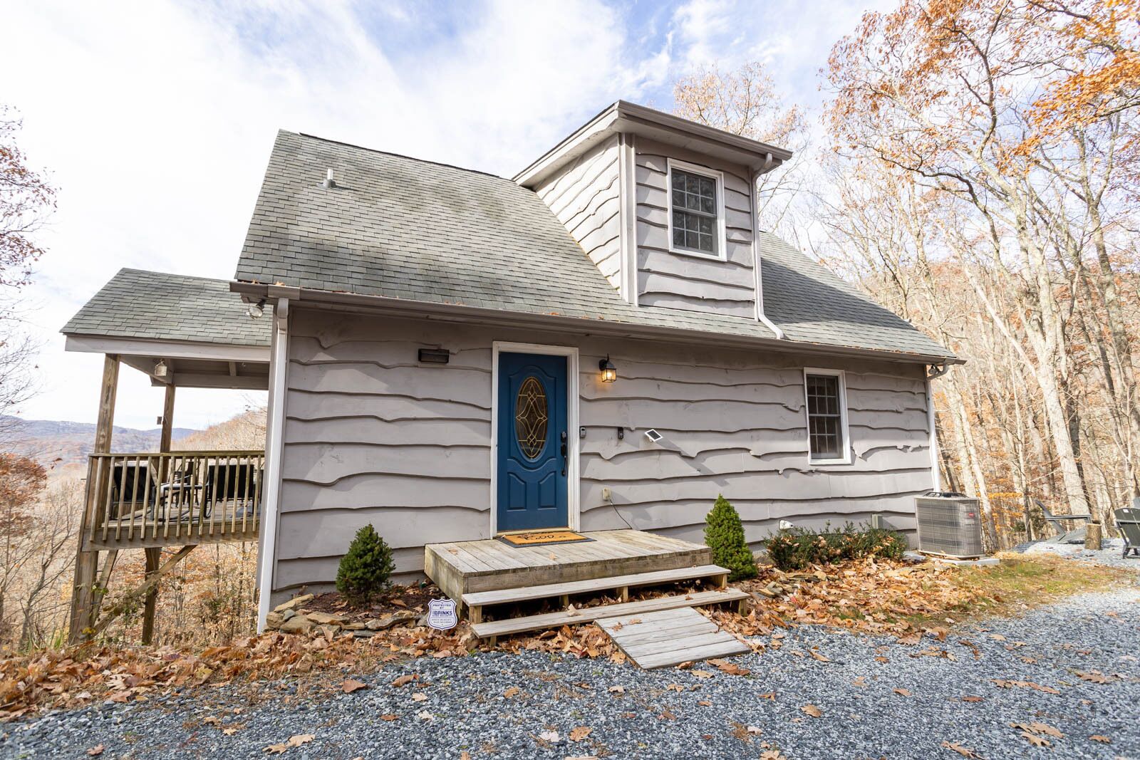 A two-story house with a blue door, a small porch, and a gravel driveway.