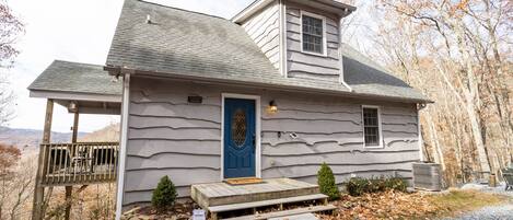 A two-story house with a blue door, a small porch, and a gravel driveway.