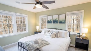 Un dormitorio con cama, mesitas de noche, ventilador de techo y ventanas grandes.