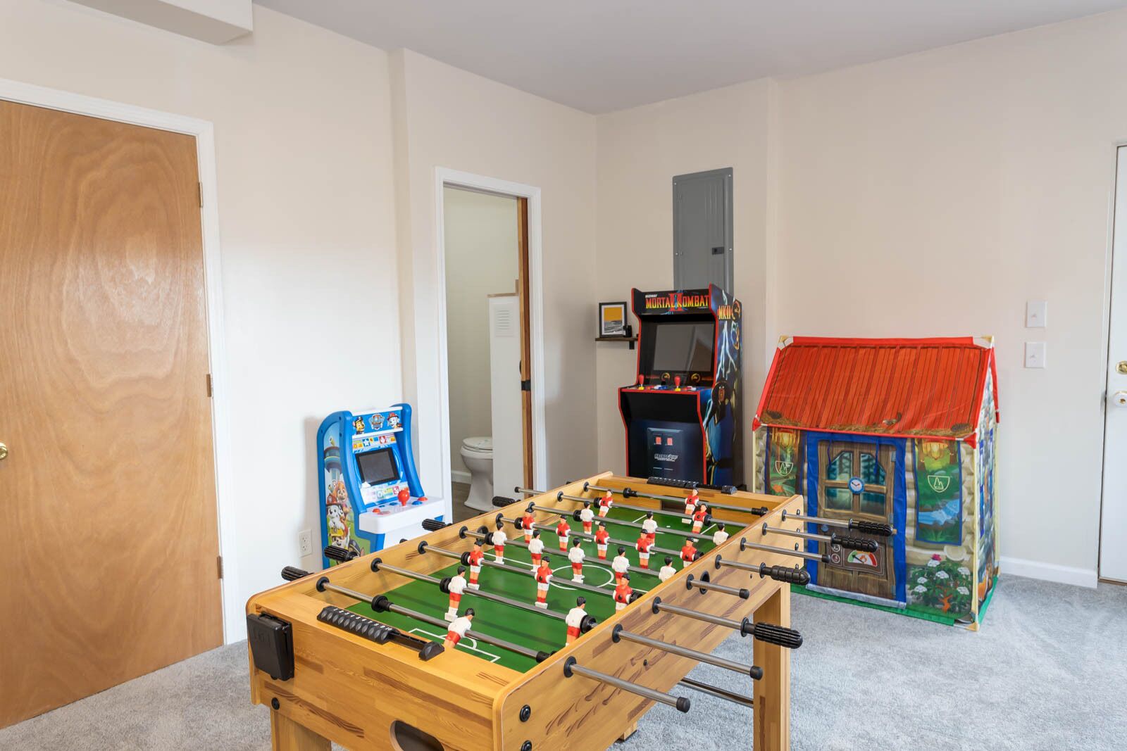 A room with a foosball table, two arcade games, and a small playhouse.