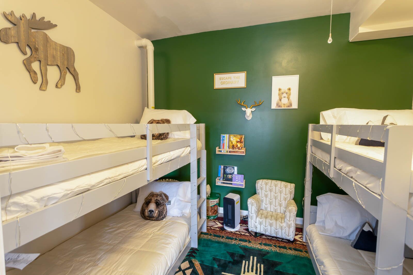 A room with bunk beds, a dog, a moose decoration, a chair, and a wall with framed pictures and a sign.