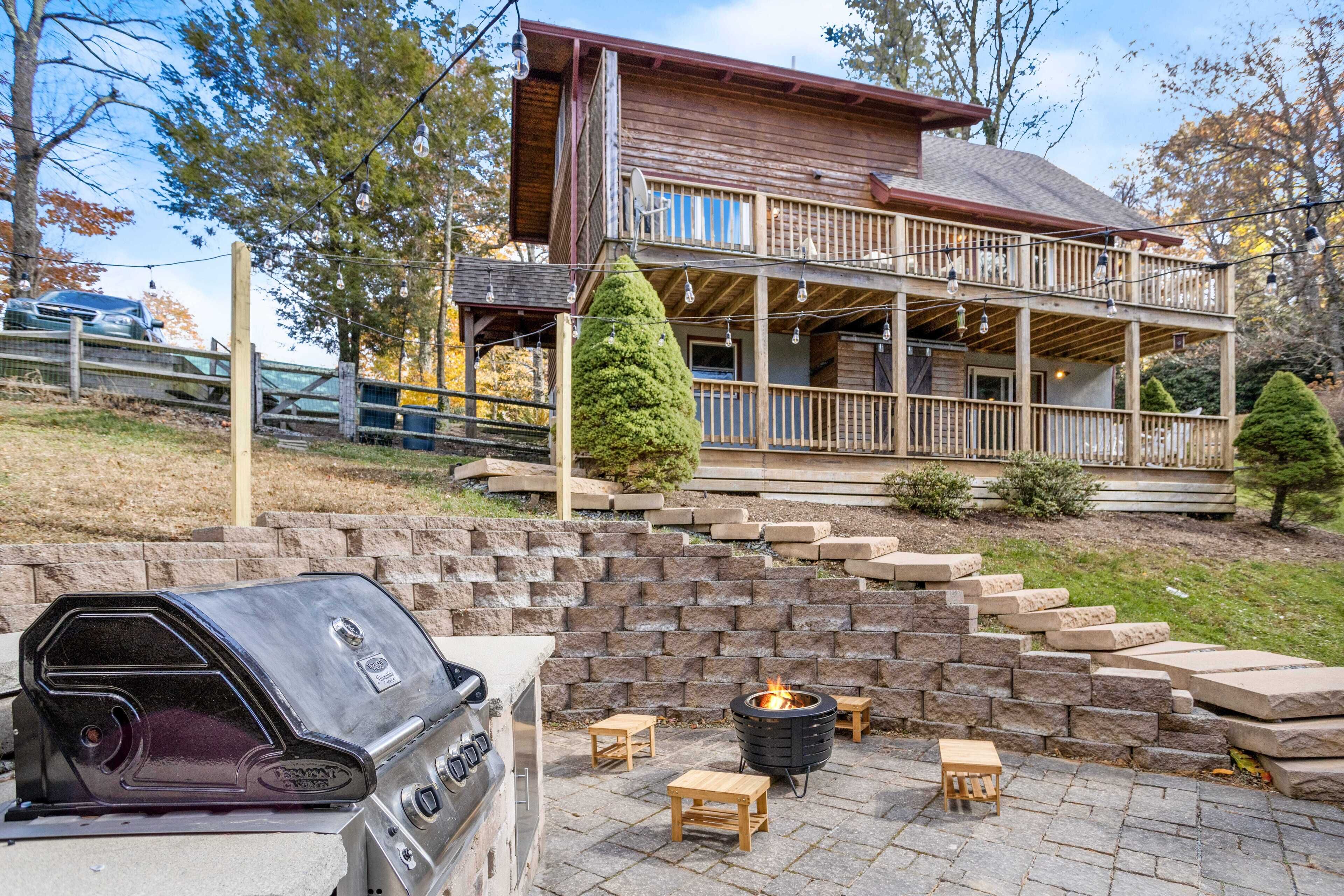 A wooden house with a deck, a barbecue grill, and a fire pit.