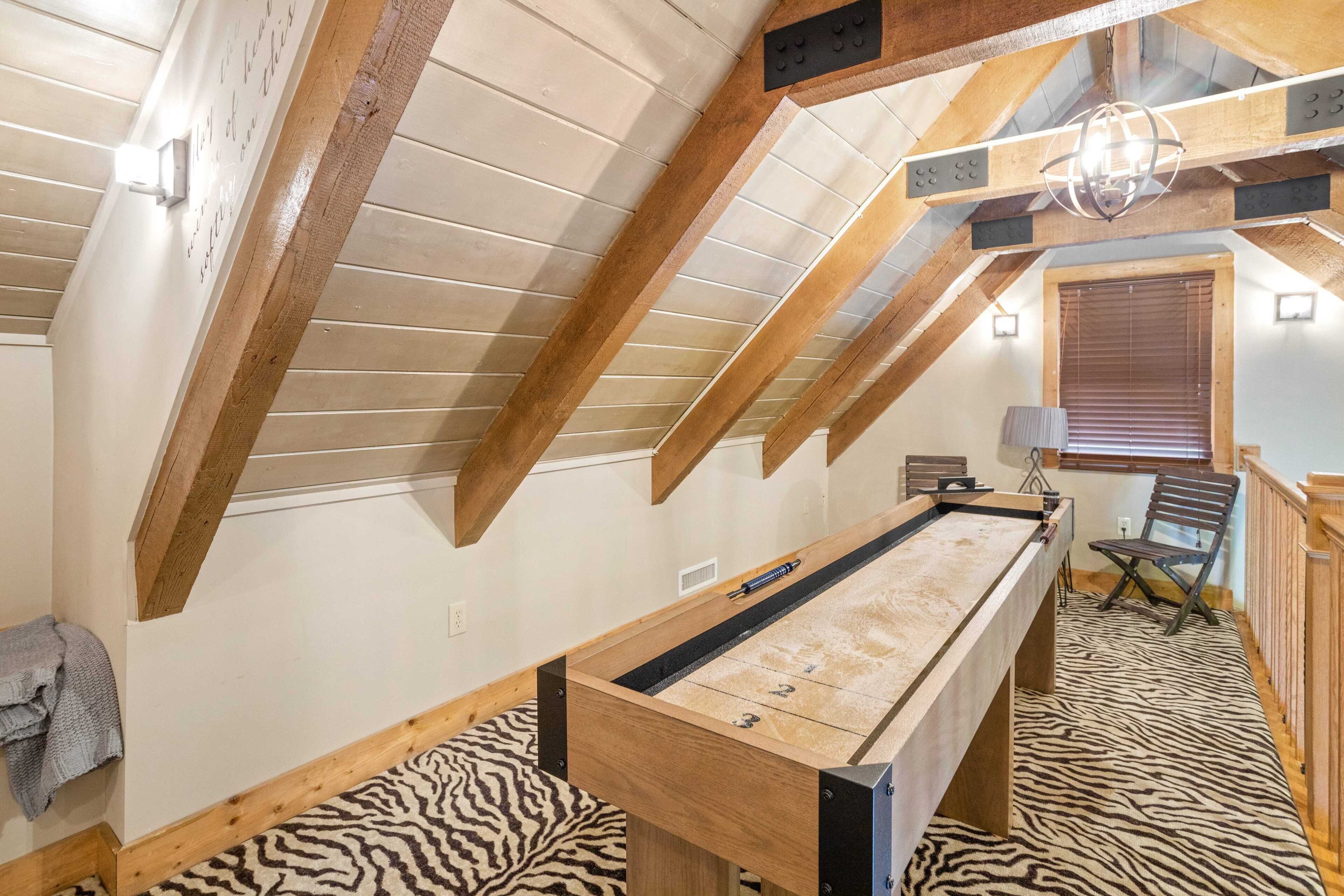 Una habitación con mesa de billar, vigas de madera, alfombra con estampado de cebra y una ventana con persianas.