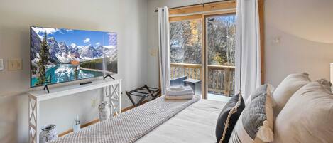 A bedroom with a bed, a TV, a window with curtains, and a view of mountains.